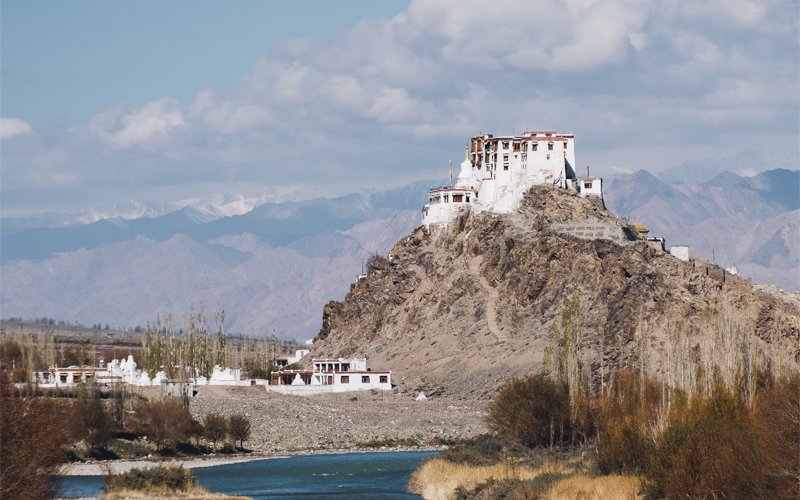 Tibetan monastery perched atop a rocky hill overlooking a river valley.